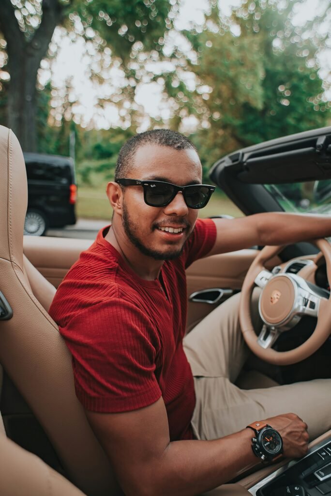 man in red crew neck shirt wearing black sunglasses sitting on driver seat